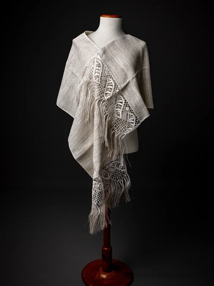 Fular o chal de encaje de Camariñas hilo color tostado y blanco con tela de lino natural y flecos, colgado de un maniquí sobre fondo negro, artesanía de Galicia.